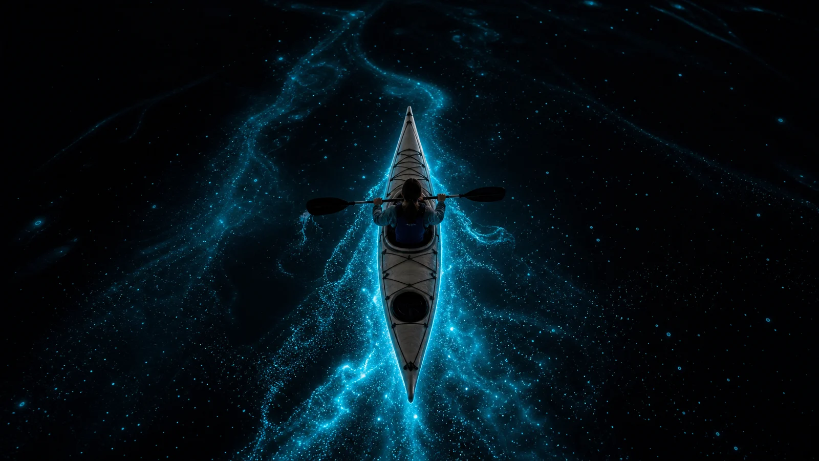 Kayaker paddling through bright bioluminescent water at dusk